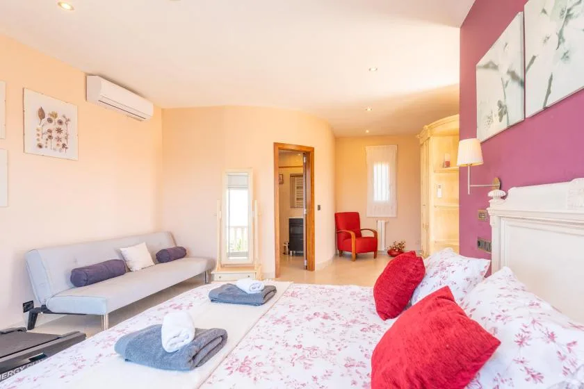 Un dormitorio luminoso con una cama, un sofá y una silla roja.
