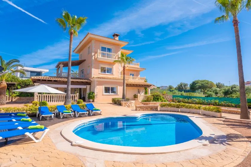 Una piscina está frente a una casa de varios pisos bajo un cielo azul despejado.