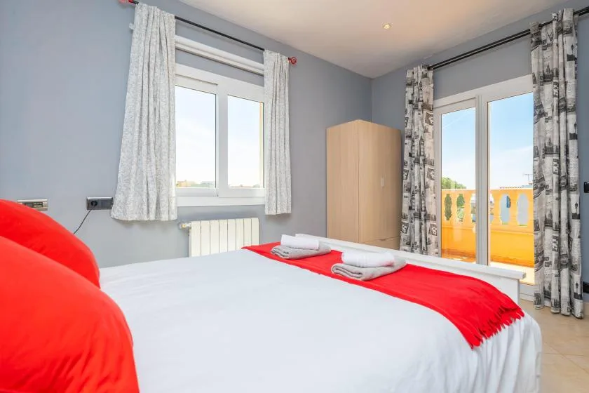 Un dormitorio con una cama bien tendida y ventanas con vistas a edificios cercanos.