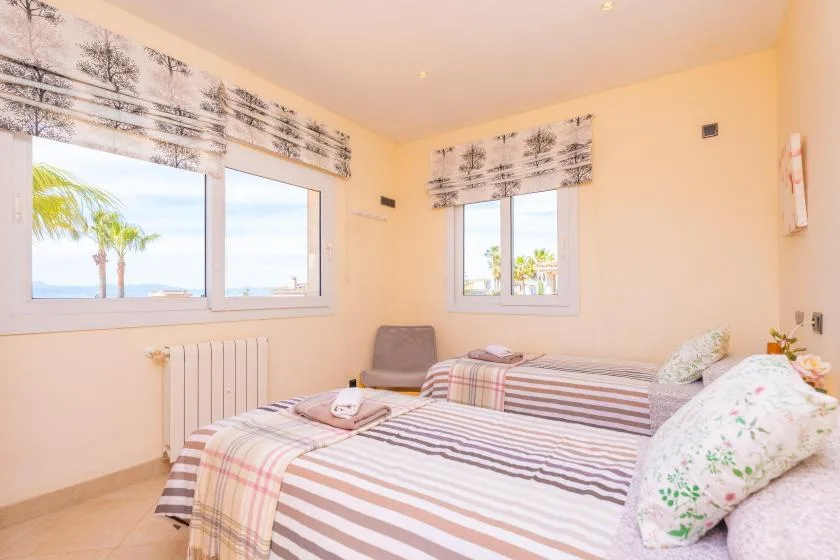 Un dormitorio luminoso con ropa de cama a rayas y ventanas con vistas a palmeras.