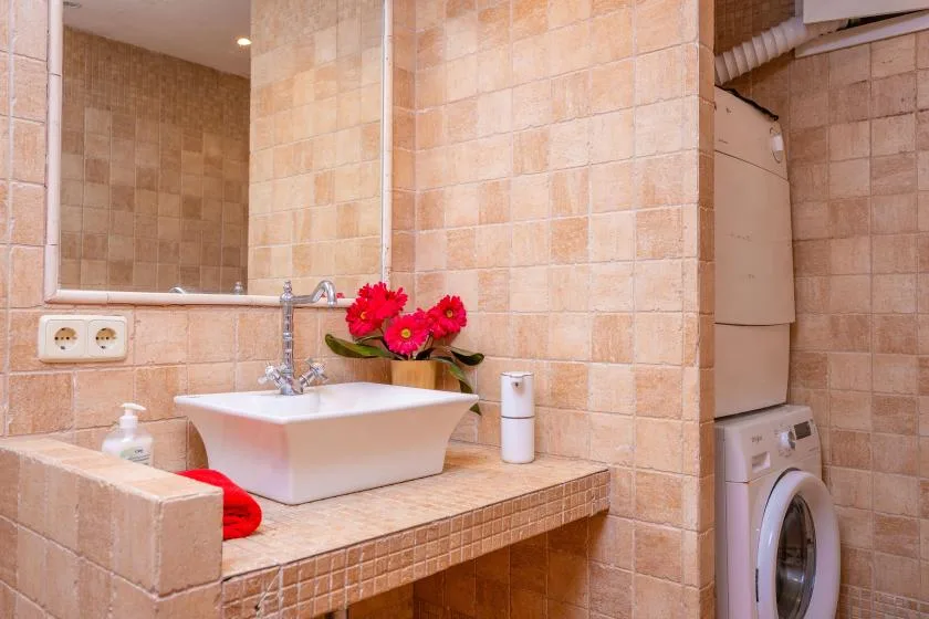 Un baño con azulejos, un lavabo, flores y una lavadora.
