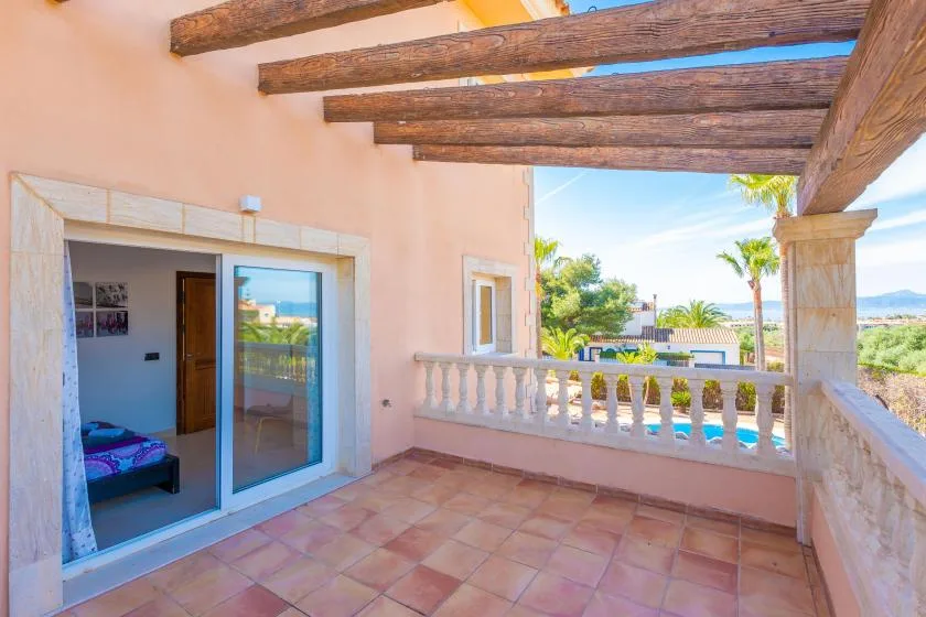 Una terraza cubierta con suelo de baldosas, vigas de madera y una puerta corredera de cristal.