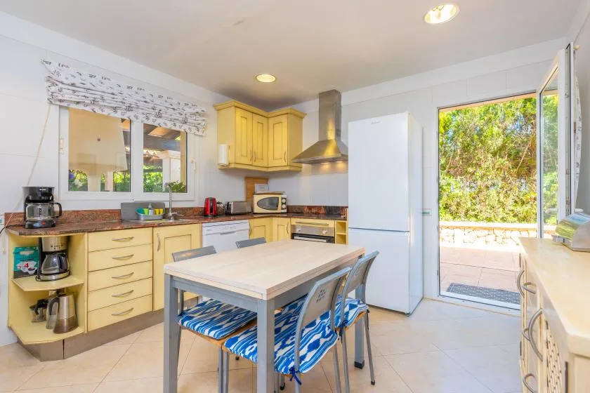 Una cocina luminosa con gabinetes amarillos, una mesa central y una puerta abierta al patio.