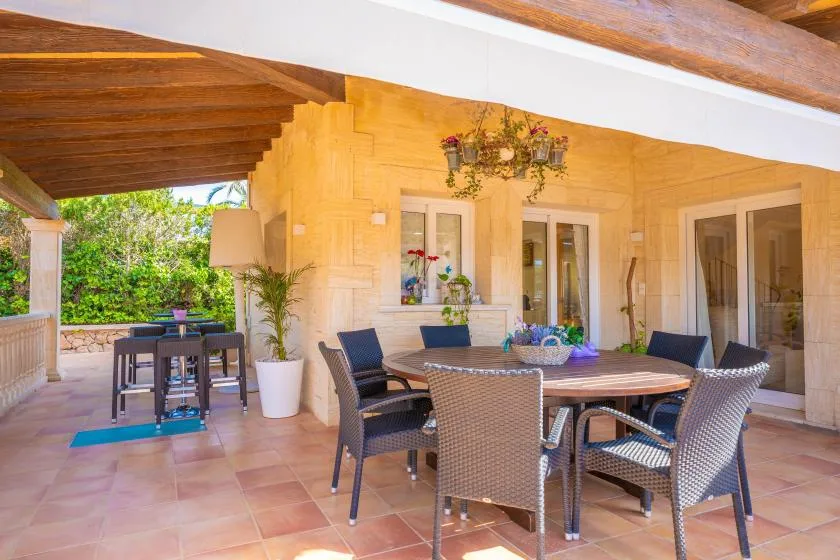 A covered patio with a dining table and chairs beside a garden.