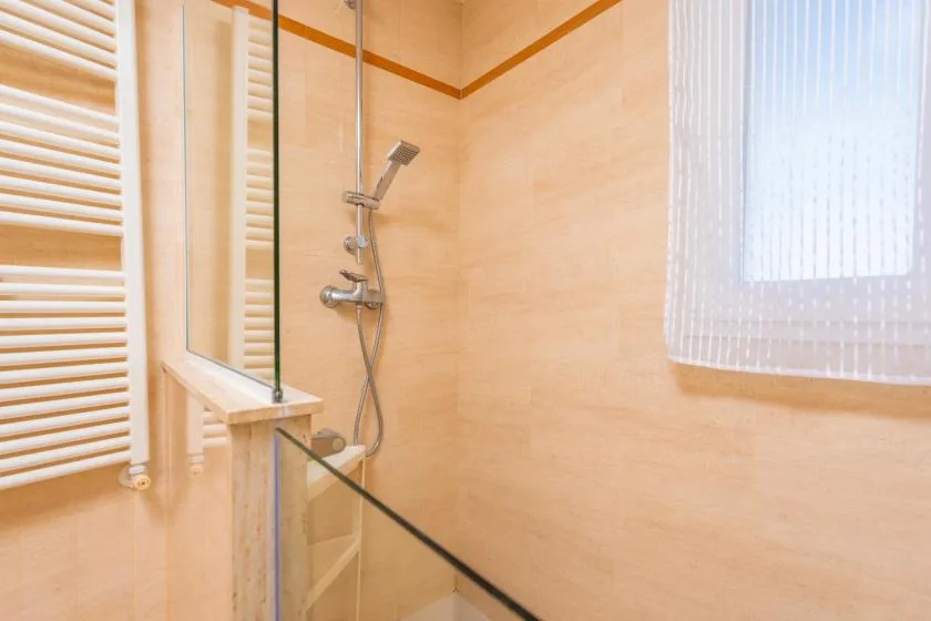 Un baño con azulejos, una ducha de vidrio y una ventana con cortina translúcida.