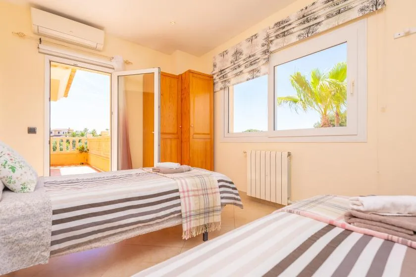 Un dormitorio con ropa de cama a rayas, un armario y ventanas con vistas a palmeras.
