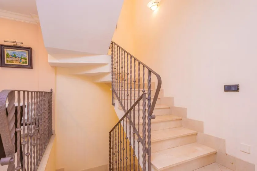 Una escalera interior con peldaños claros y barandillas decorativas oscuras.