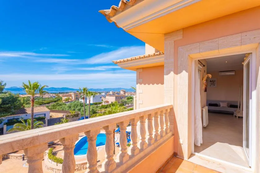 Un balcón soleado ofrece vistas a una piscina, casas cercanas y la costa a lo lejos.