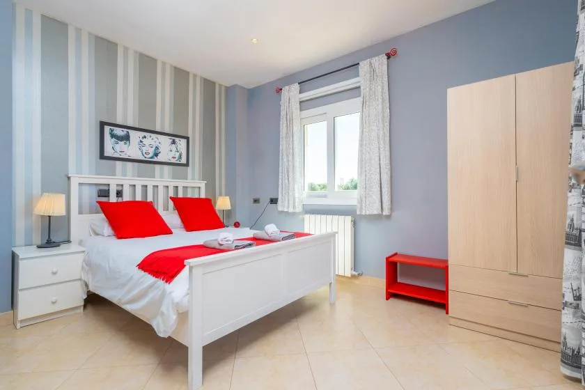Un dormitorio con una cama blanca, ropa de cama roja y un armario de madera clara.