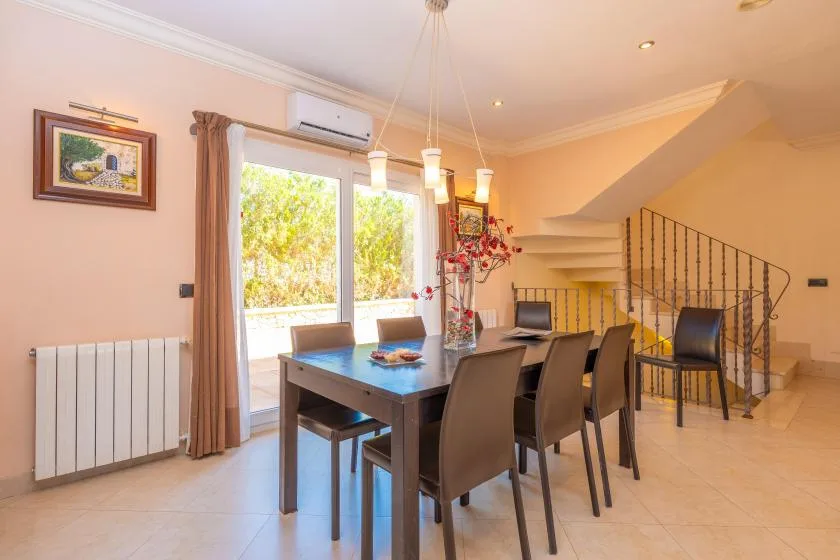 Un comedor con una mesa larga junto a grandes ventanas y una escalera.