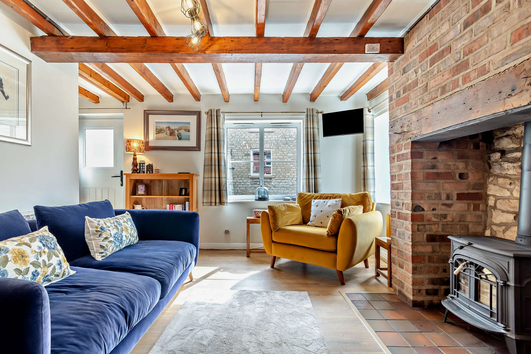 A living room with blue and mustard seating beside a brick fireplace.
