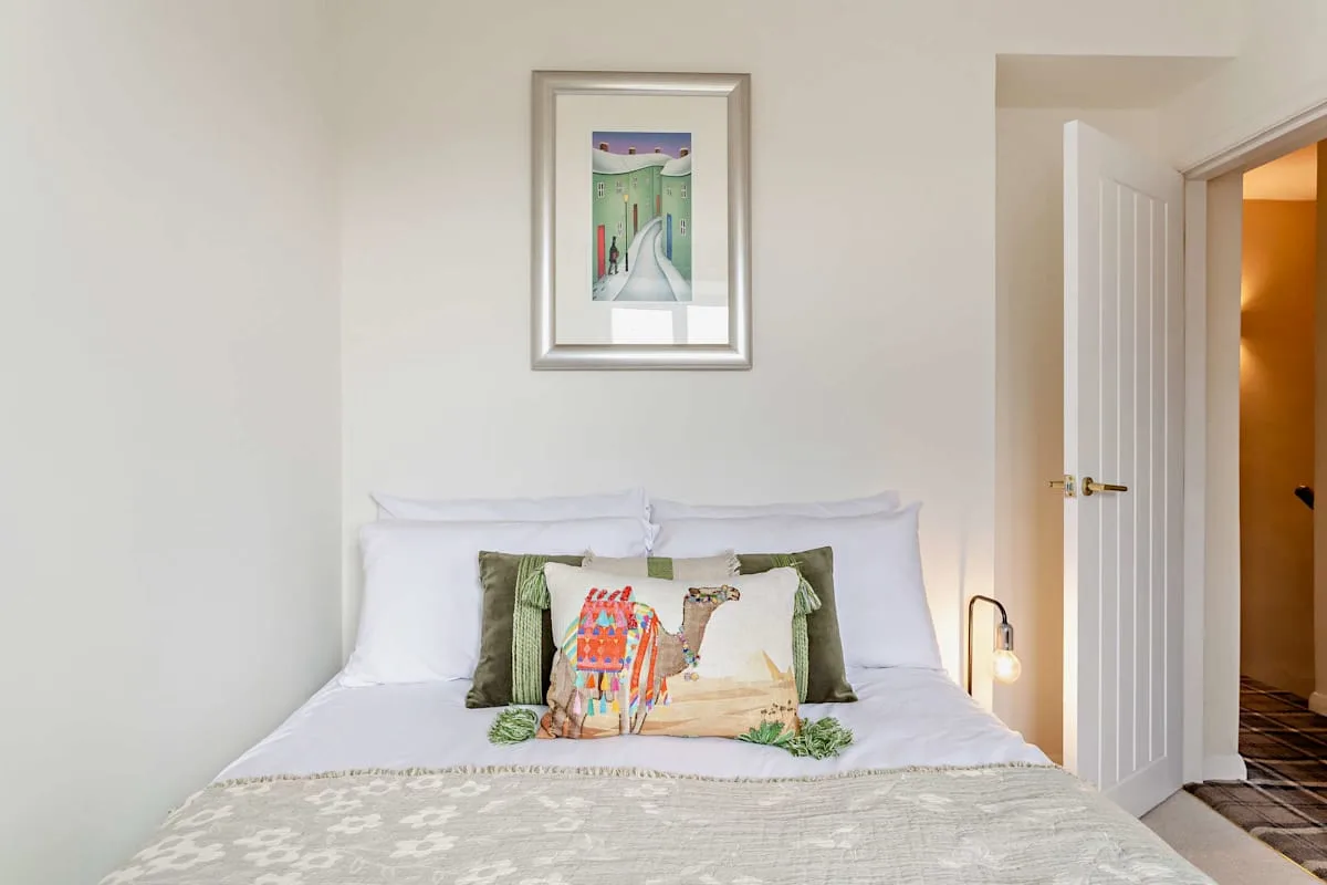 A bedroom with a neatly made bed and framed artwork above it.