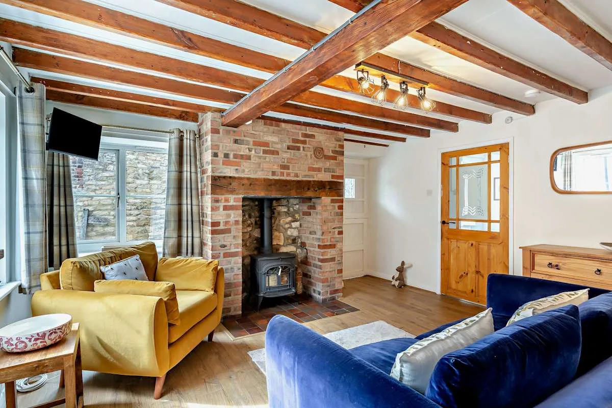 A living room with exposed wooden ceiling beams and a brick fireplace.