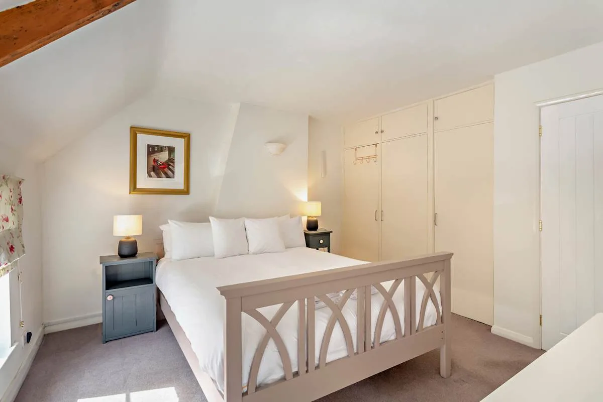 A bedroom with a bed, bedside tables, and built-in cupboards.