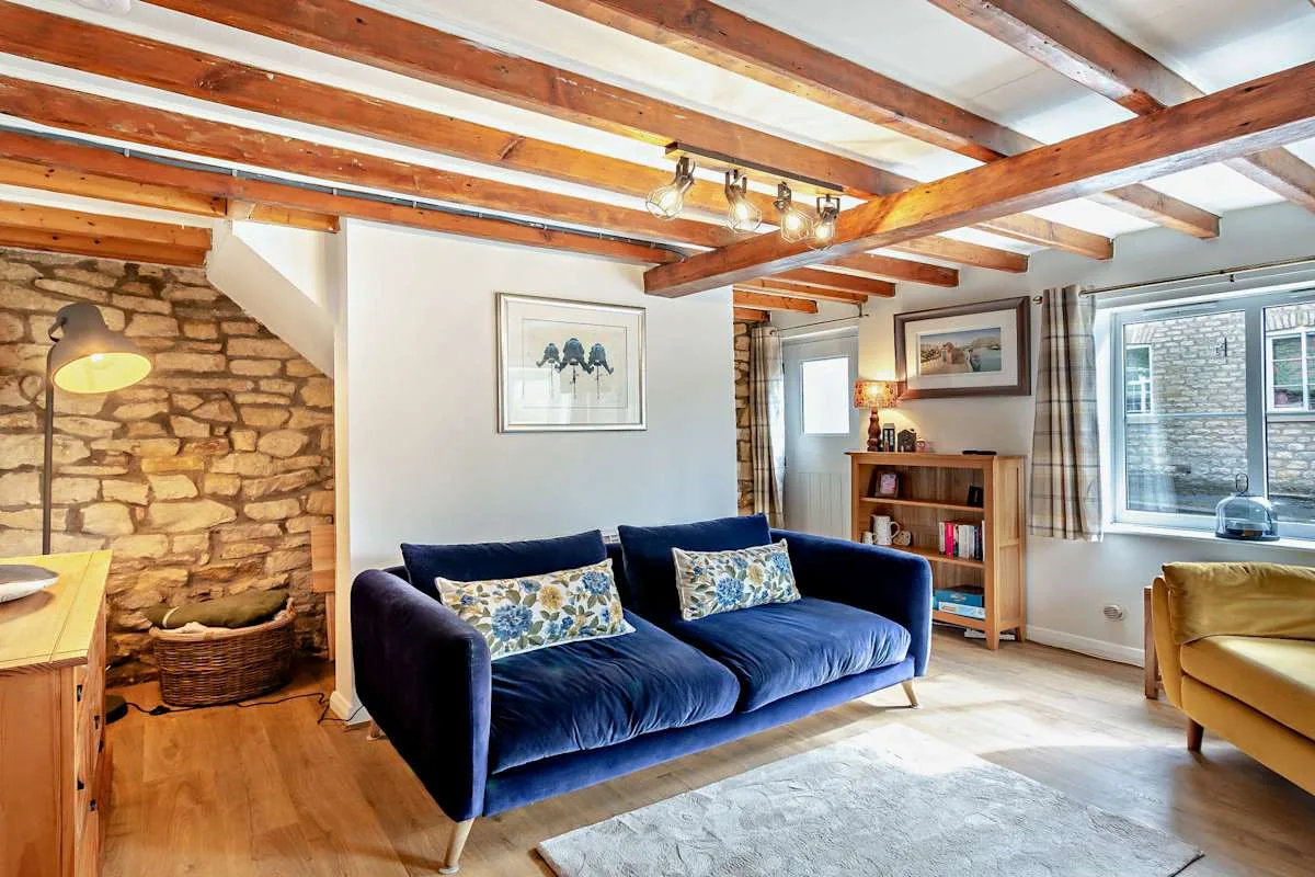 A living room with blue seating, exposed beams, and a stone fireplace.