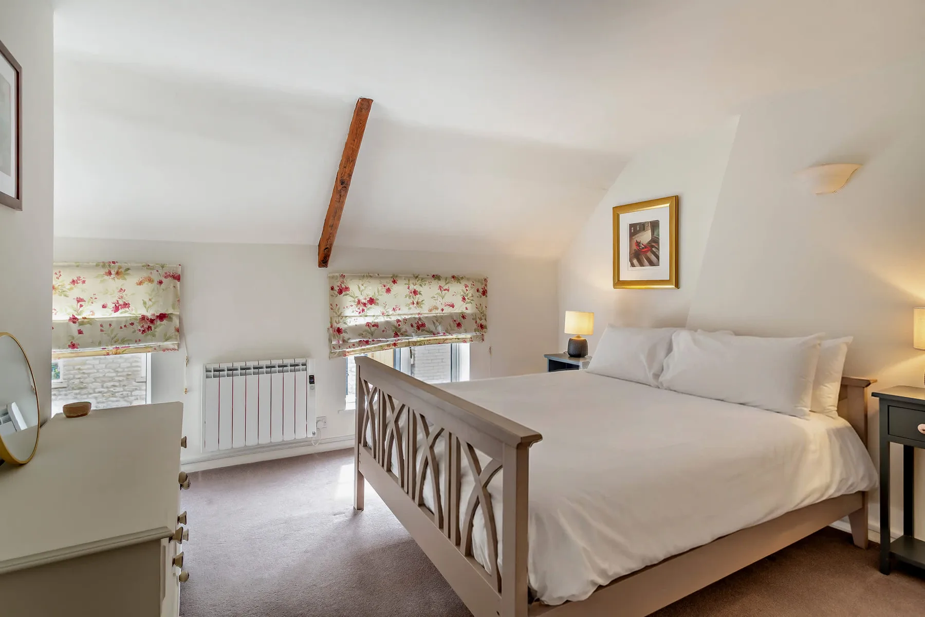A bright bedroom with a large bed, floral window shades, and a sloped ceiling.