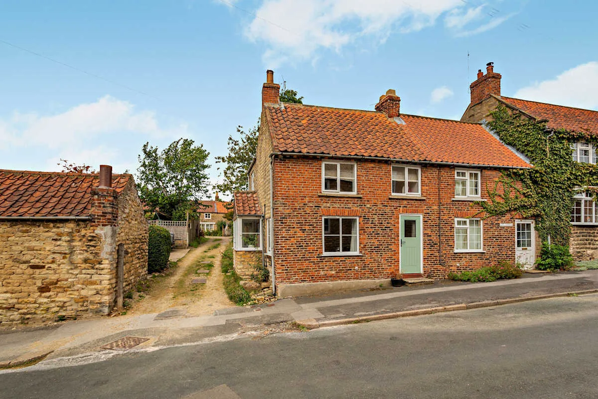 A brick cottage stands beside a narrow lane and a stone wall.