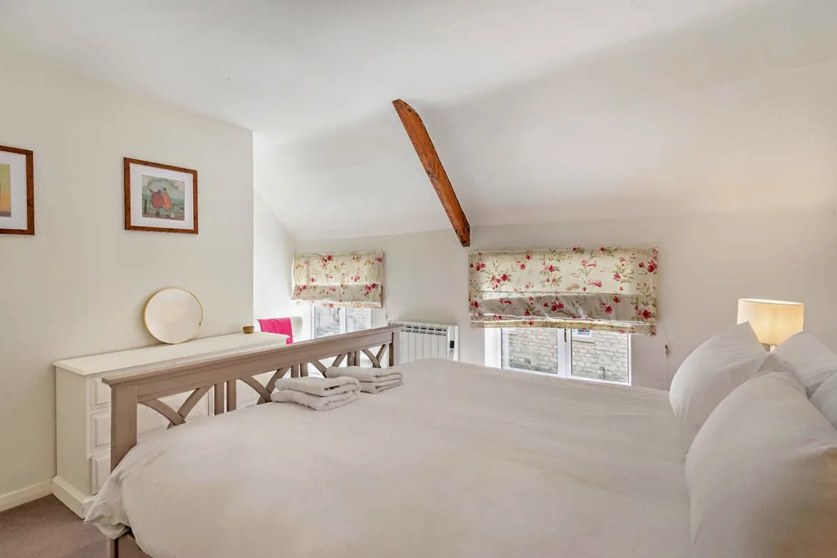 A bright bedroom with a bed, floral window curtains, and a sloped ceiling.