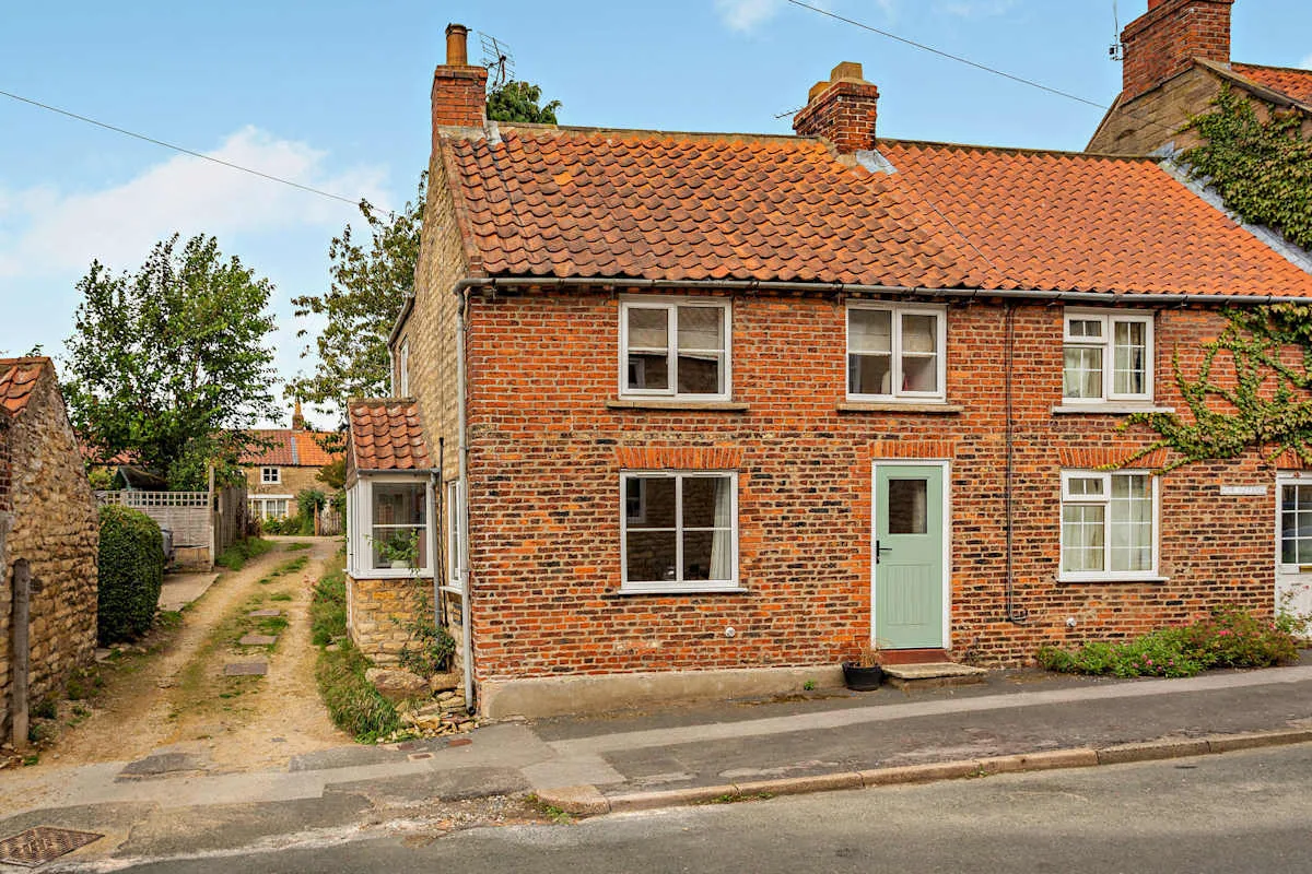 A brick cottage faces a narrow lane, with a pale green front door.