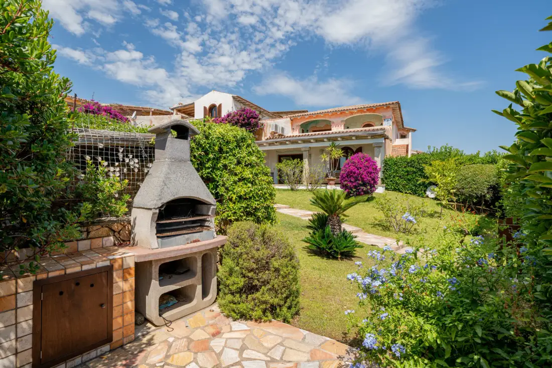 Una casa y un jardín con una barbacoa exterior junto a un patio de piedra.