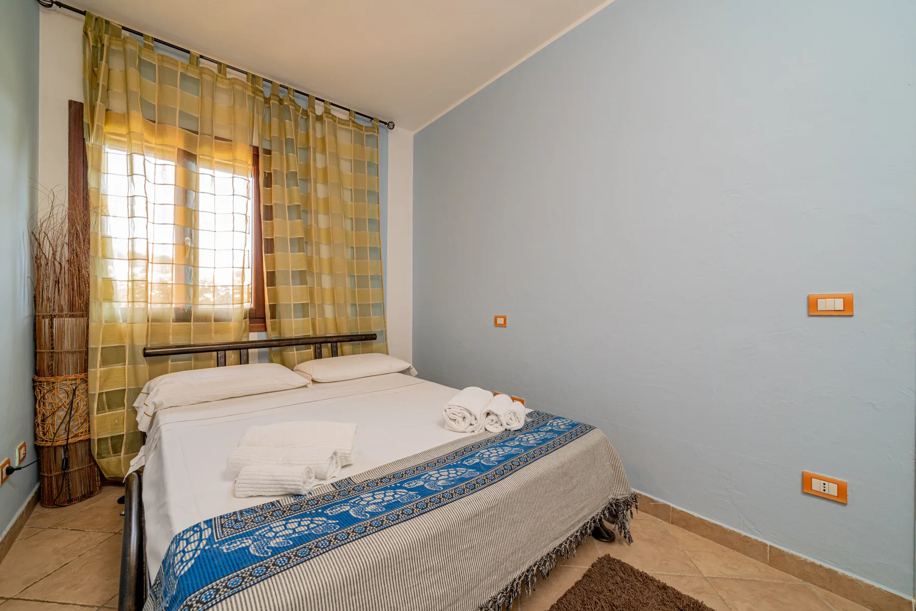 Un dormitorio con una cama bien tendida bajo una ventana con cortinas estampadas.
