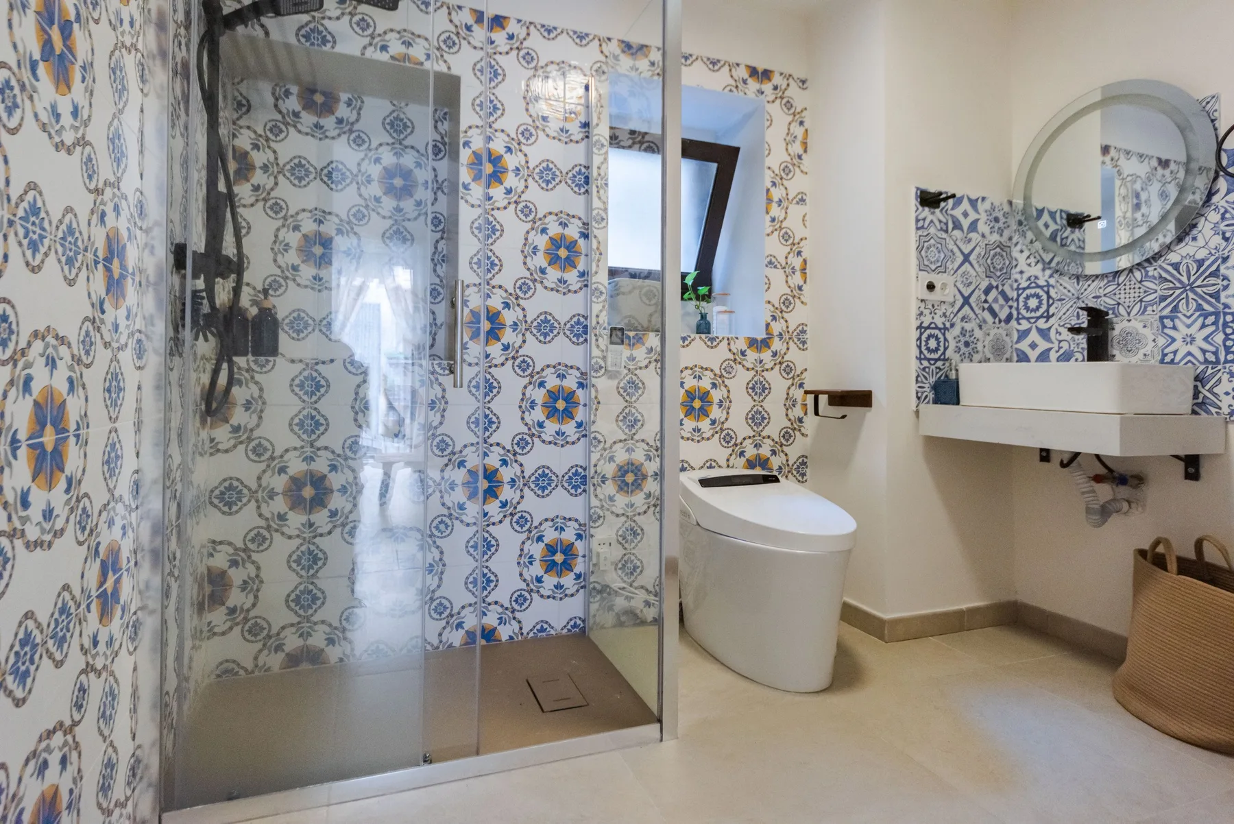Un baño con ducha de vidrio, azulejos estampados y un lavabo suspendido.