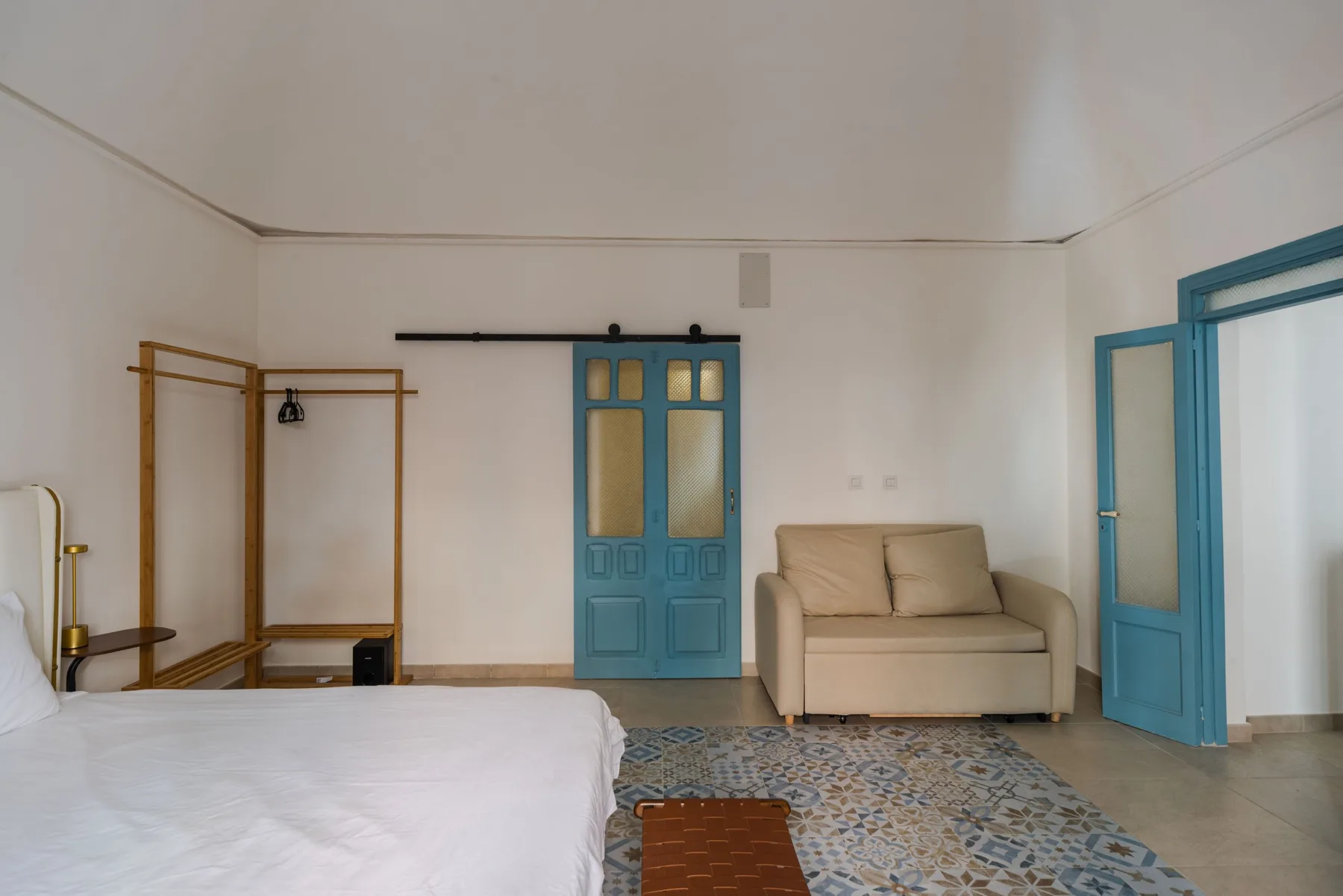 Un dormitorio con una cama, una zona de estar beige y puertas azules.