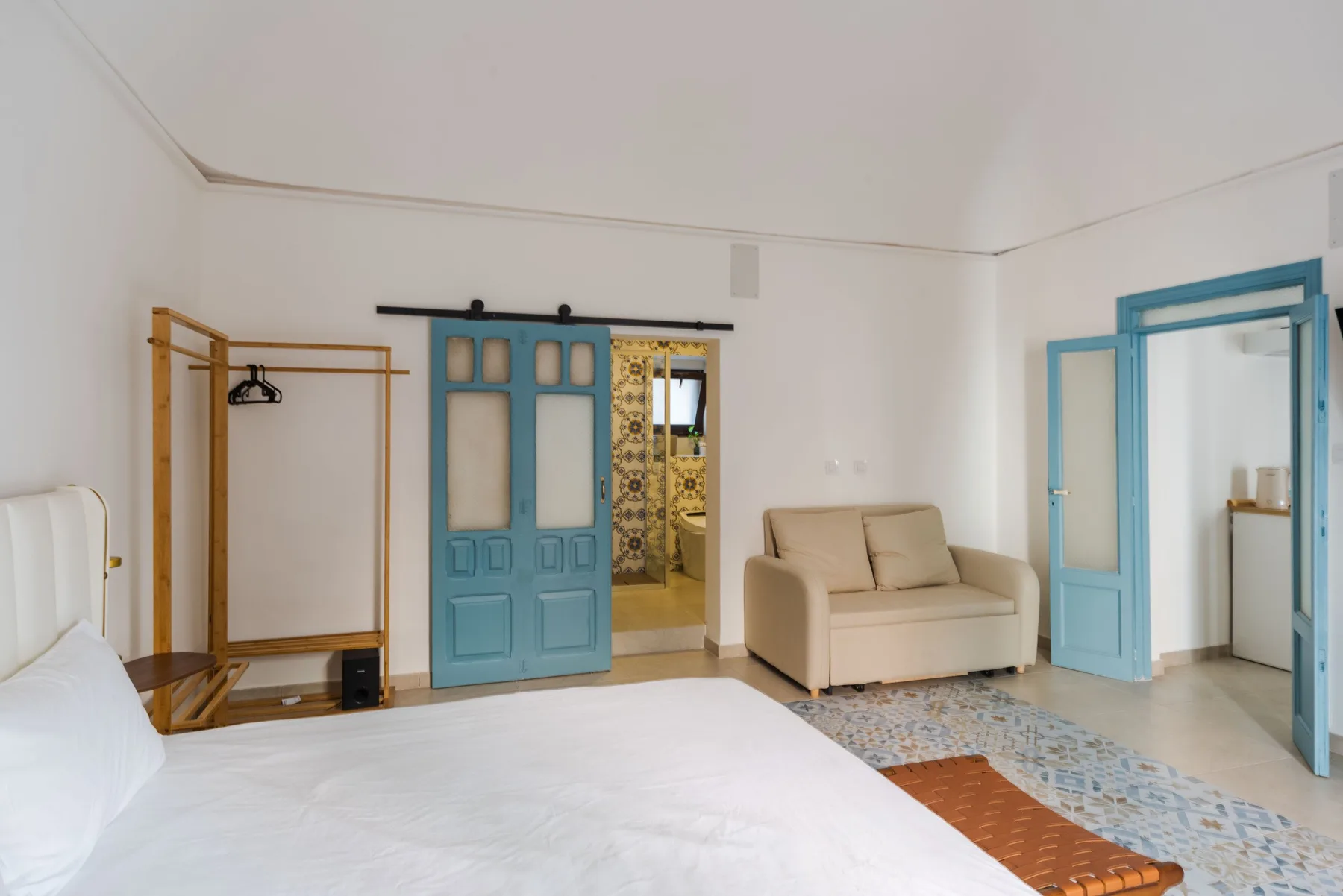 A bright bedroom with a bed, beige seating, and blue-framed doorways.