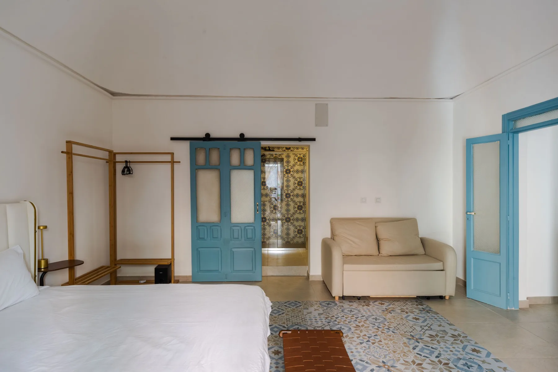 Un dormitorio con una cama, una zona de asiento beige y puertas azules.