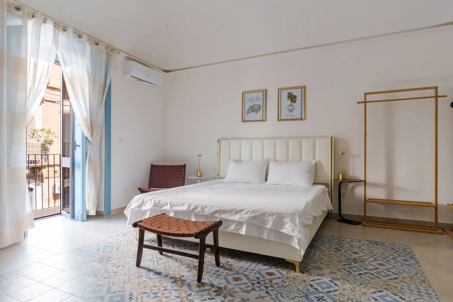 Un dormitorio luminoso con una cama bien arreglada y cortinas junto a la puerta del balcón.