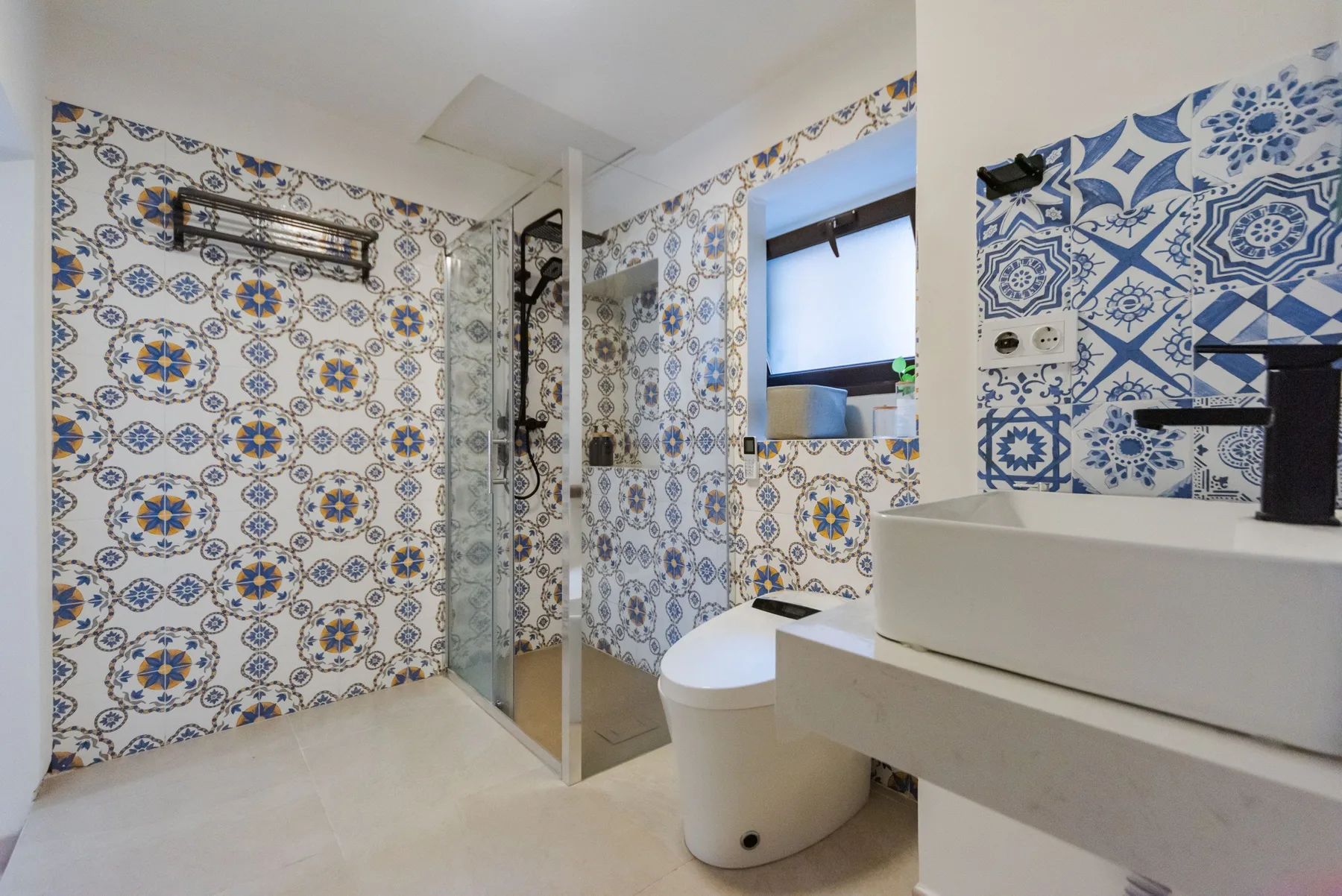 Un baño con azulejos estampados azules y blancos, ducha, inodoro y lavabo.