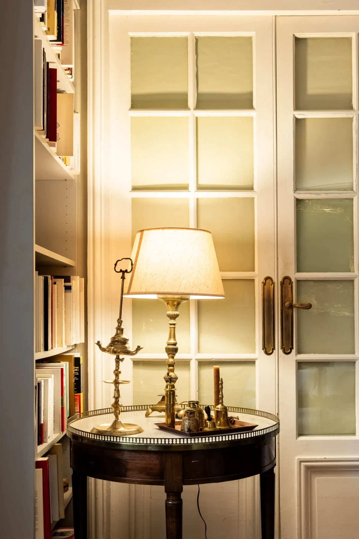A warmly lit reading nook features a small round table beside a bookcase and glass-paneled doors.