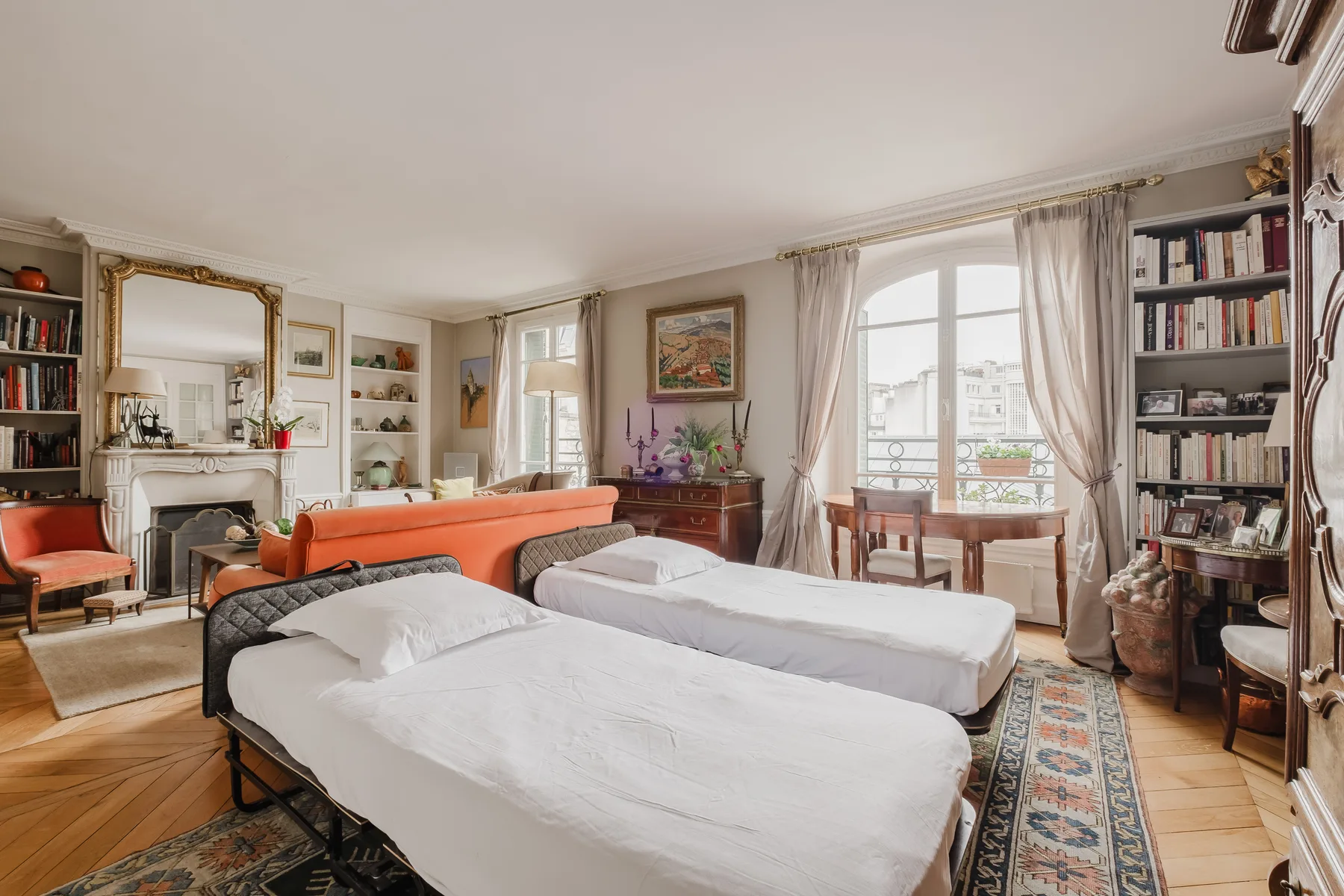 A bright bedroom with two beds, bookshelves, and a small dining table by the window.