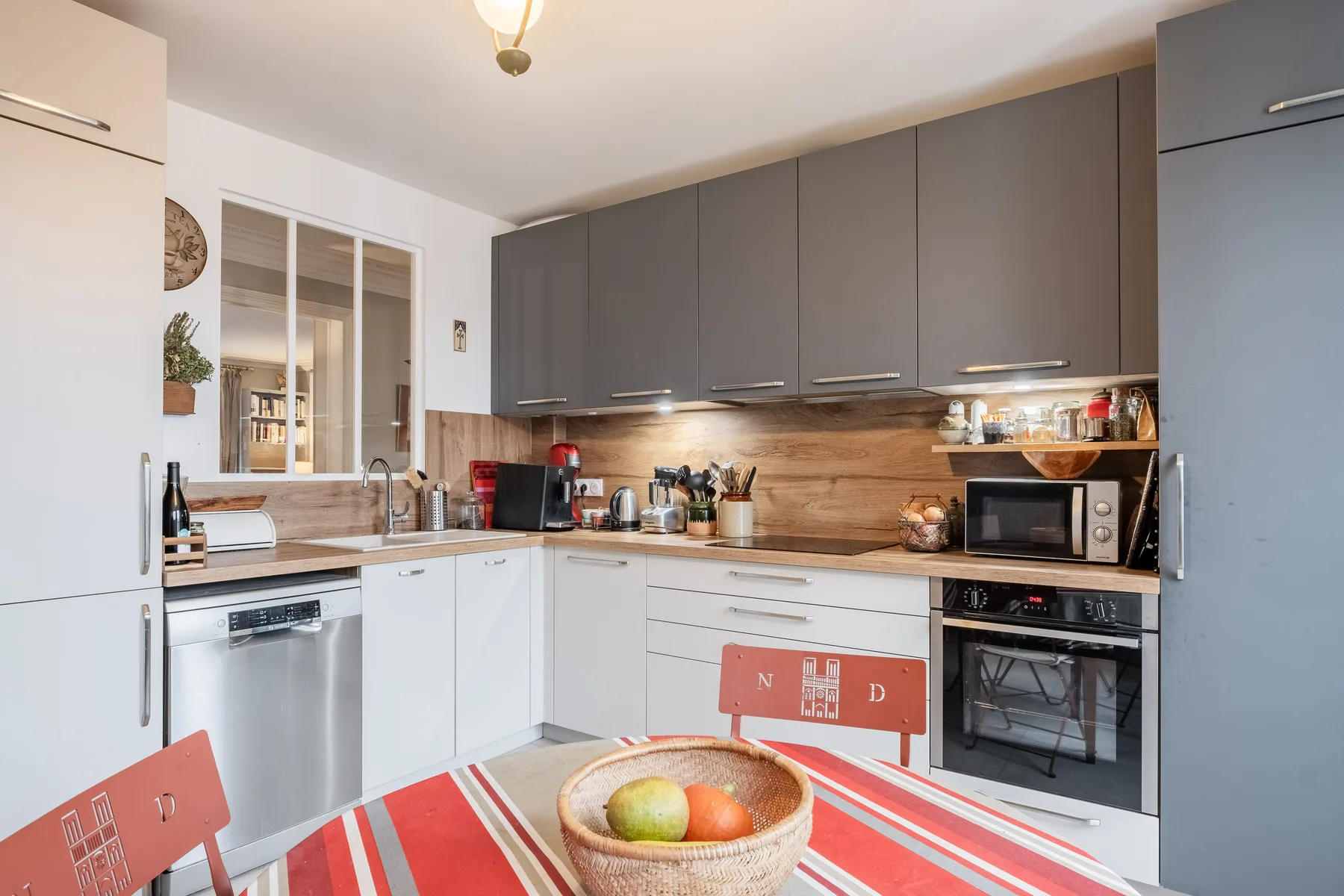 A modern kitchen with gray cabinets, white cupboards, and a striped tablecloth.