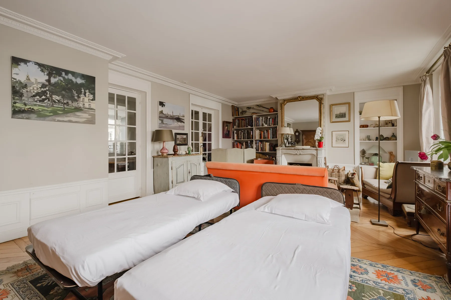 A bedroom with two beds, an orange sofa, and a bookshelf.