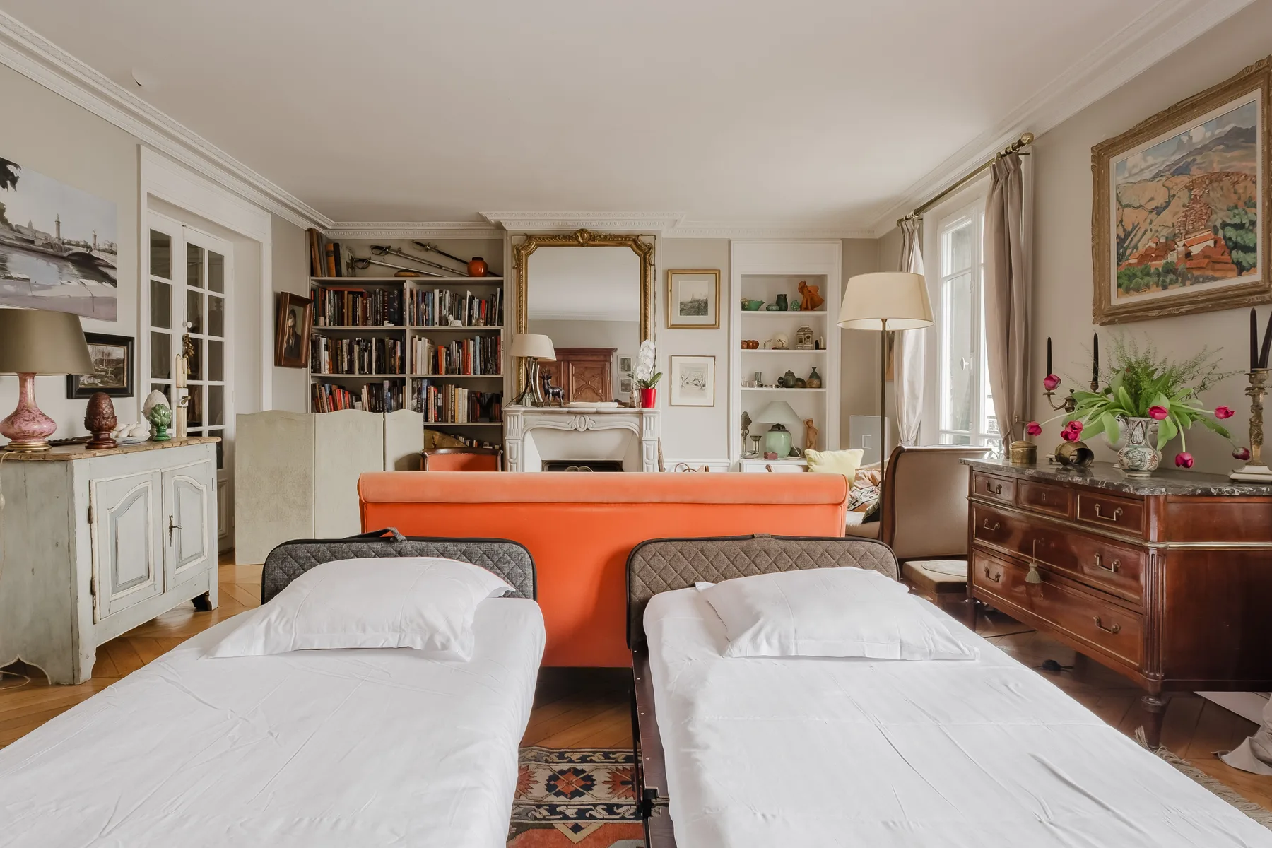 A bedroom with two beds, an orange sofa, and bookshelves.