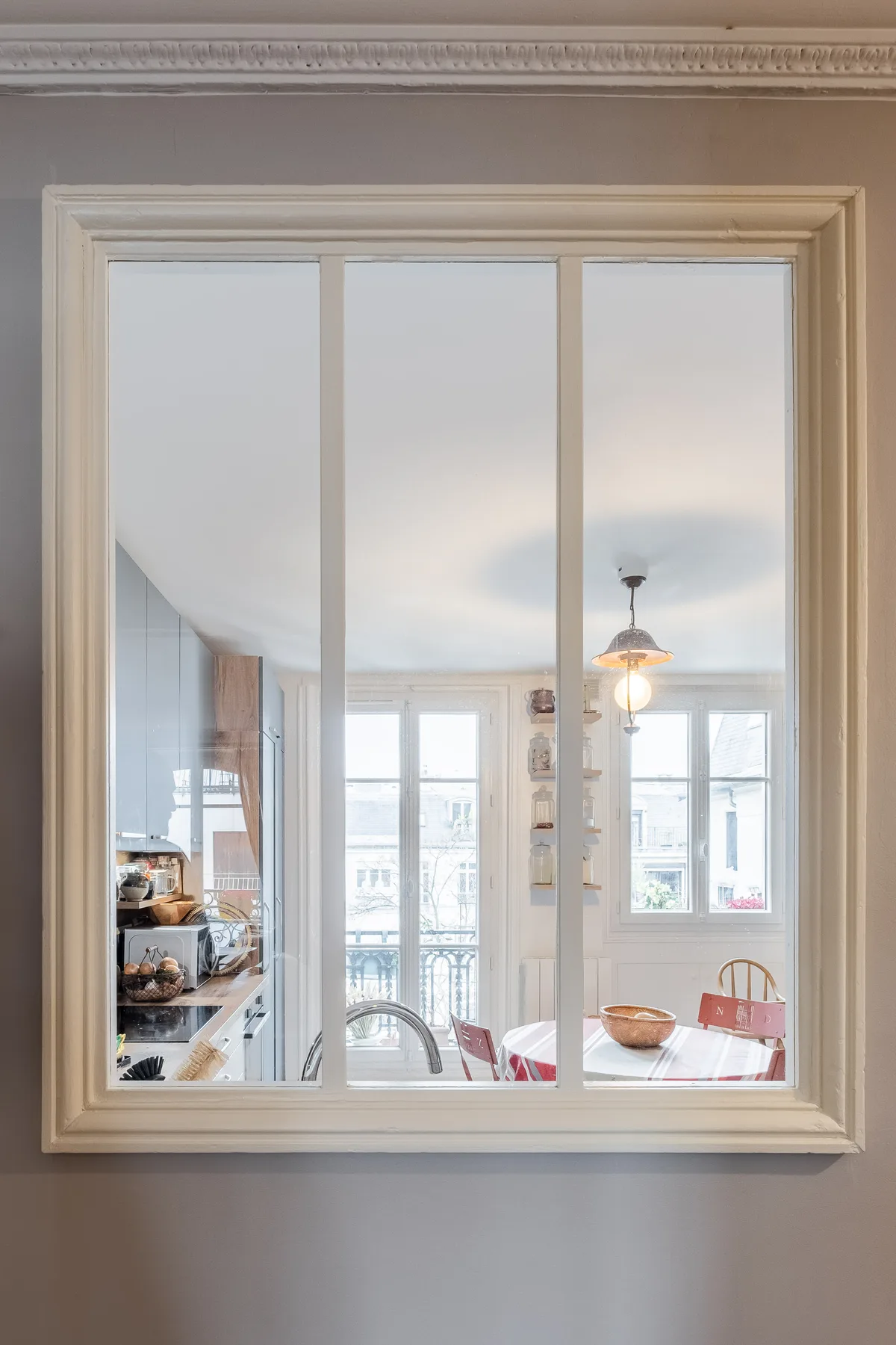A bright kitchen and dining area are visible through a large interior window.