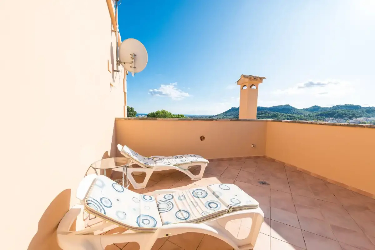 A sunny terrace with cushioned loungers and distant hills.