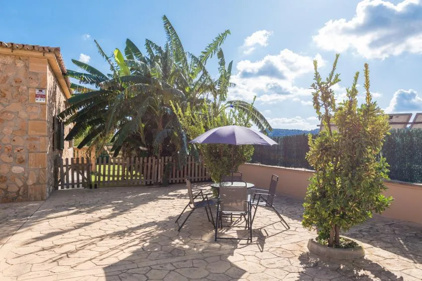 A paved outdoor patio has a table and seating beneath a sun umbrella.