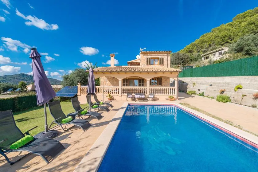 A swimming pool and patio sit in front of a house on a sunny day.