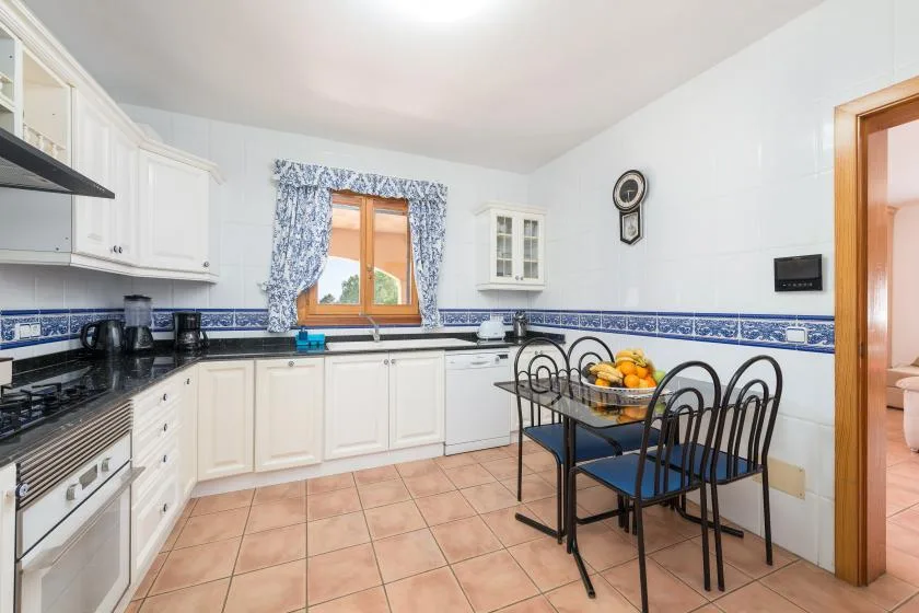 A bright kitchen with white cabinets, a tiled floor, and a dining table.
