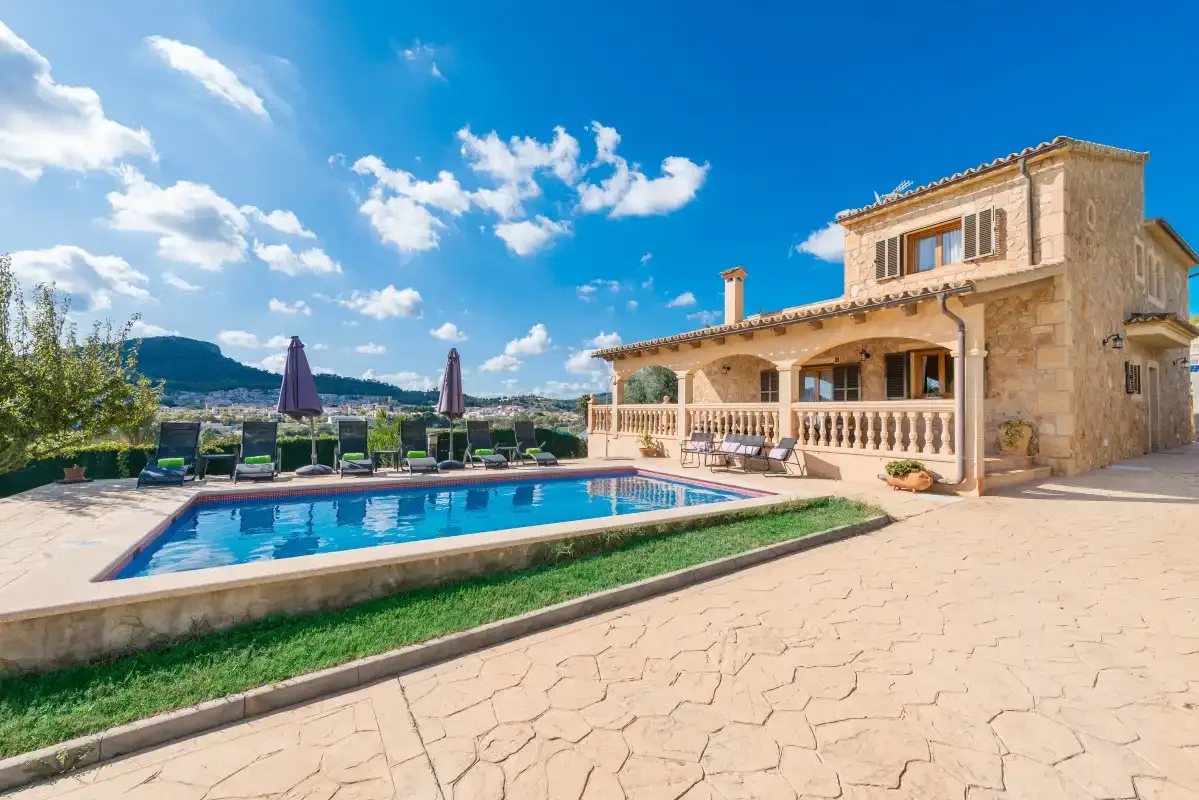 A stone house stands beside a swimming pool on a sunny patio.