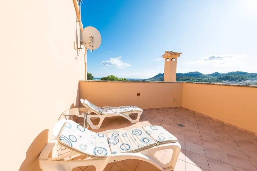 A sunny rooftop terrace has lounge seating and views of distant hills.