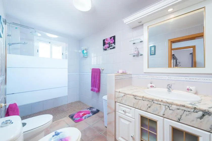 A bright bathroom with a sink vanity, large mirror, and glass shower.