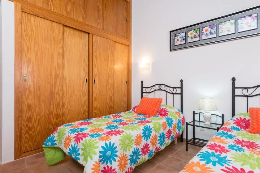 A bedroom with two beds covered in bright floral bedding beside wooden closets.