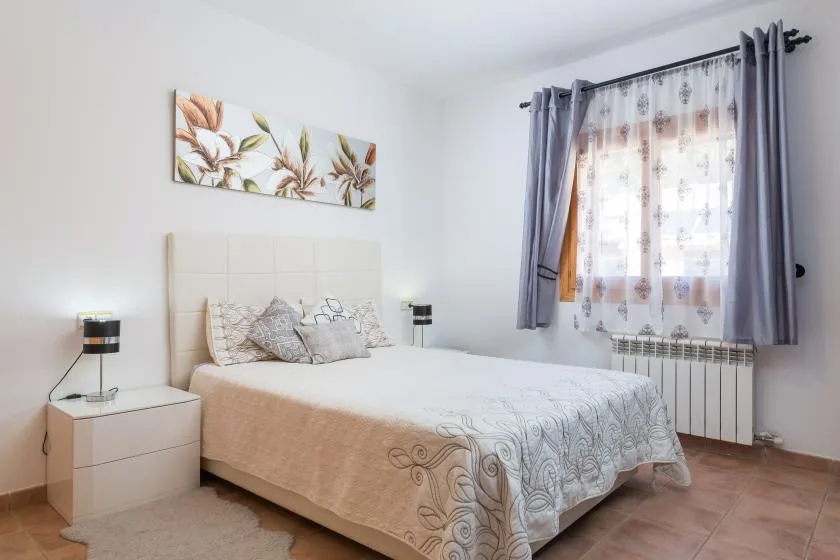 A bedroom with a bed beneath floral wall art and a curtained window.