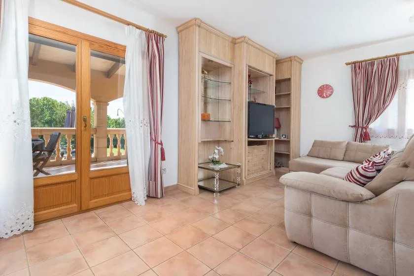 A living room with a sectional sofa, television, and wooden doors opening to a balcony.
