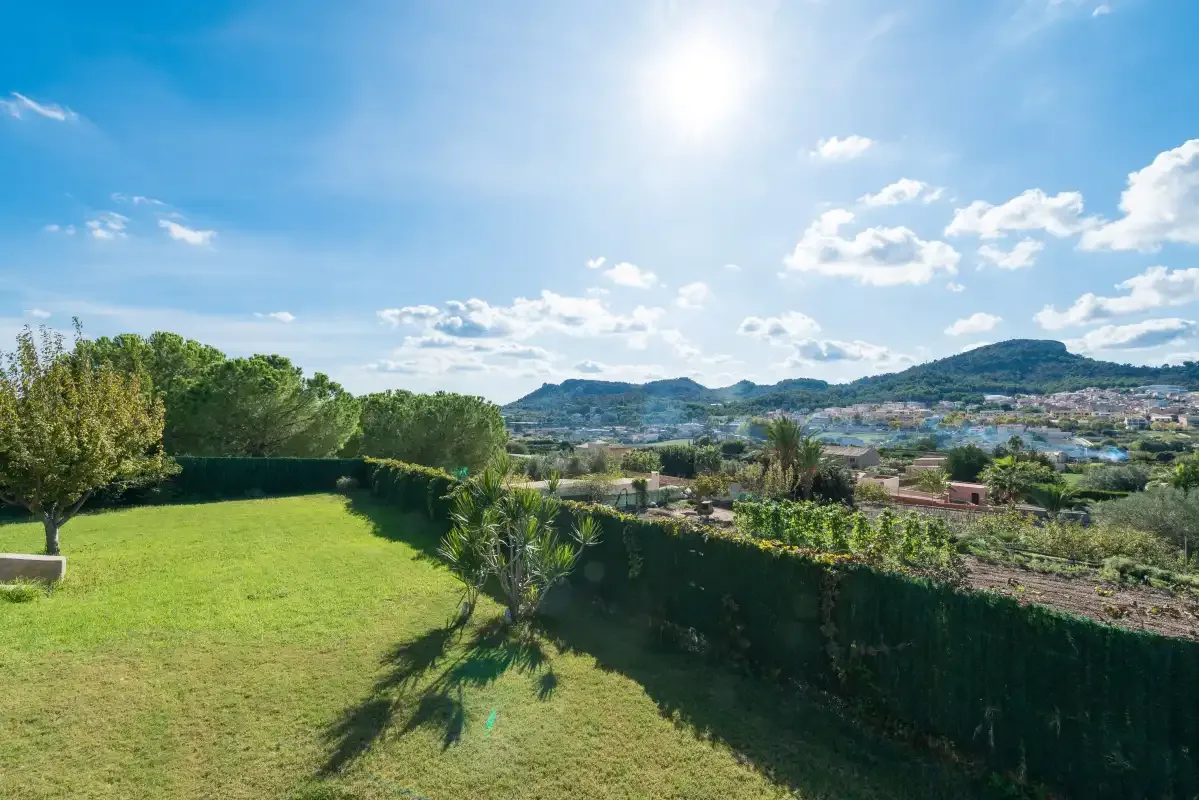 A grassy garden bordered by hedges overlooks a town and distant hills.