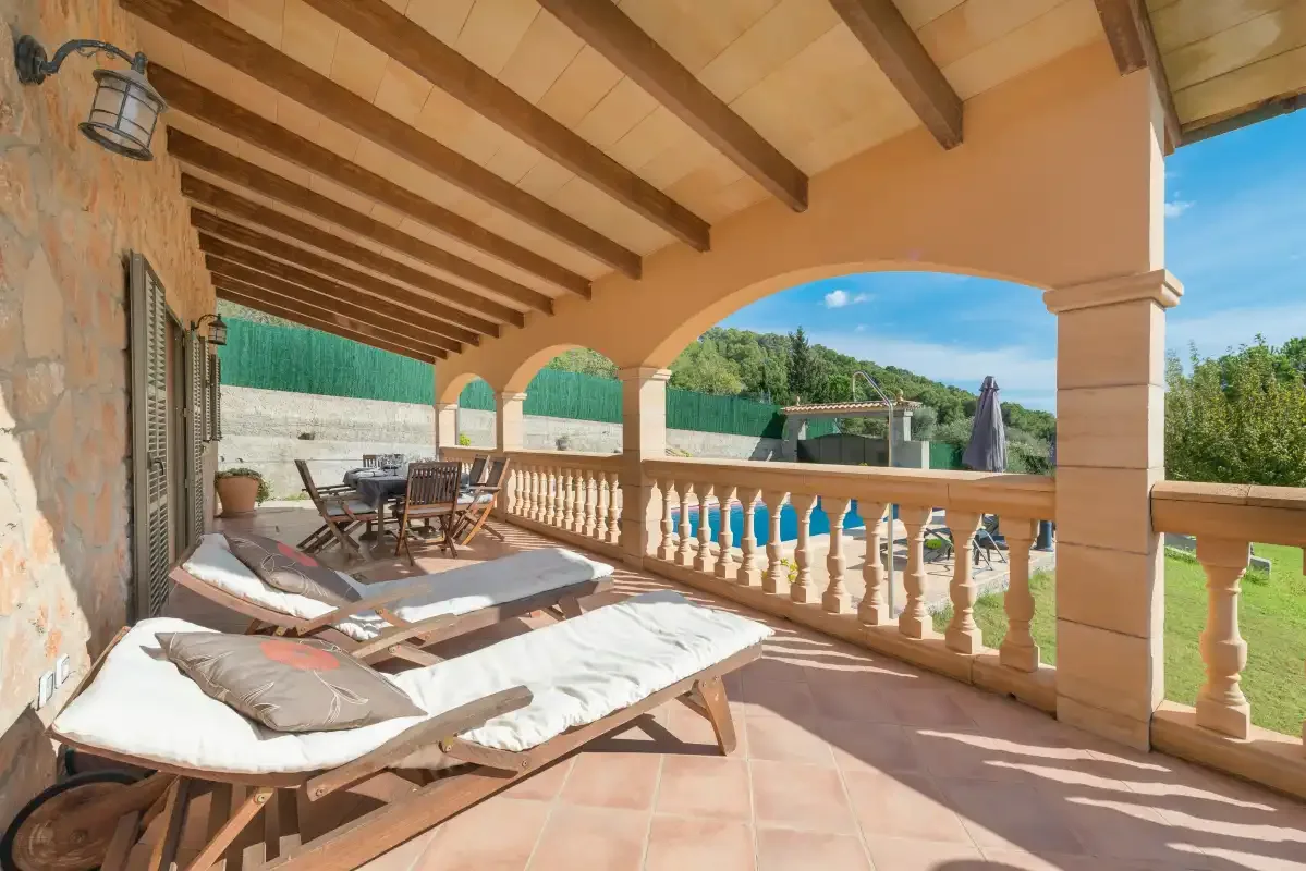 A covered outdoor terrace with cushioned seating and a balustrade overlooking greenery.
