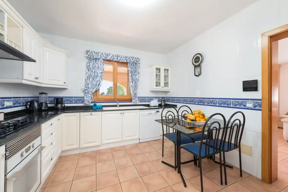 A bright kitchen with white cabinetry, blue tile trim, and a dining table.